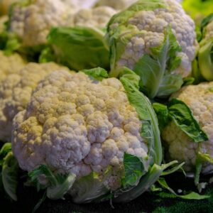 Close-up of fresh cauliflowers with green leaves at a market. Perfect for food photography.