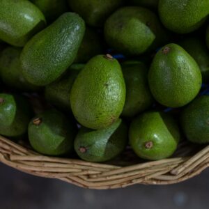 A close-up view of freshly harvested organic avocados in a wicker basket at a market.