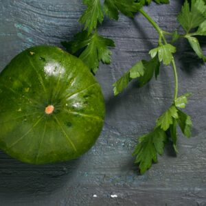 Close-up of a green pumpkin and parsley on a textured surface, highlighting nature's fresh produce.