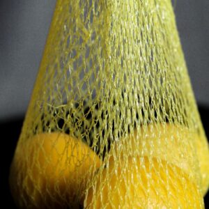 A close-up shot of fresh lemons contained in a yellow net bag, highlighting their vibrant color.