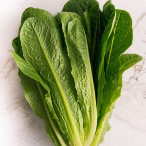 Close-up shot of vibrant green romaine lettuce leaves on a white marble surface.