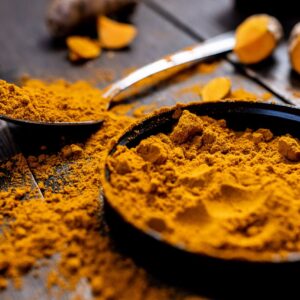 Close-up of vibrant turmeric powder with root on rustic wooden table, emphasizing texture and color.