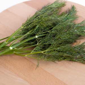 A close-up of fresh dill leaves on a wooden chopping board, ideal for food preparation.