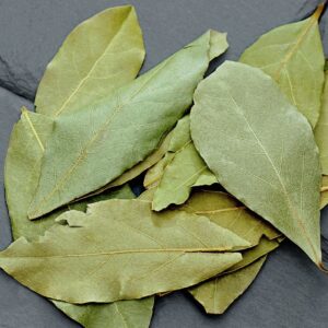 A close-up photo of dried bay leaves on a textured slate surface, ideal for spice and culinary themes.